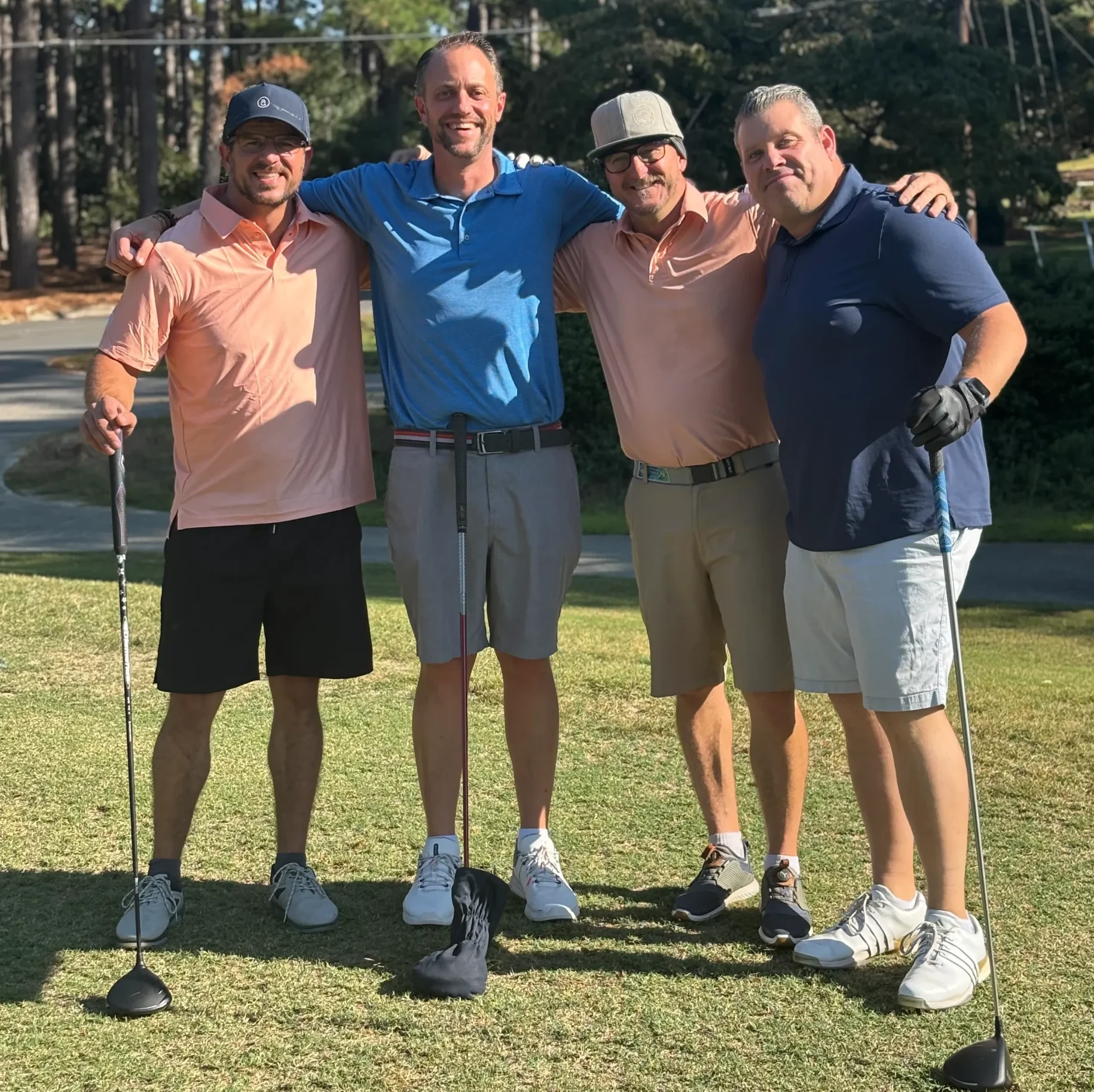 First Night at Whispering Pines: four golfers shoulder to shoulder on the tee box before the opening shot.