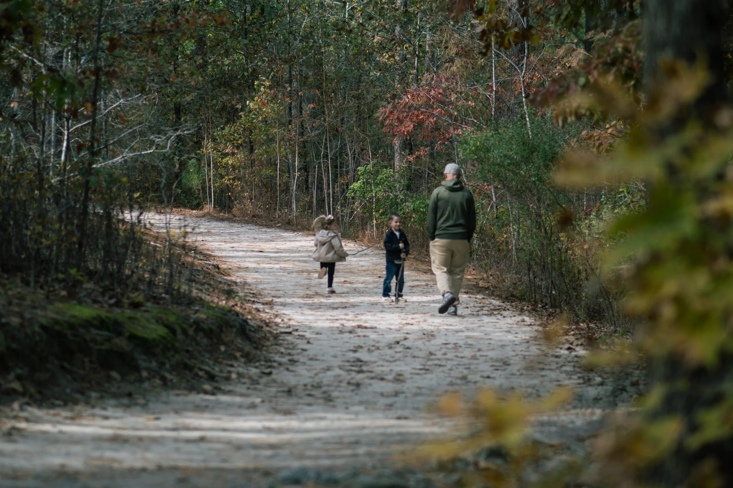 Father walking a wooded trail in fall with his children, choosing to carry less and live steady.