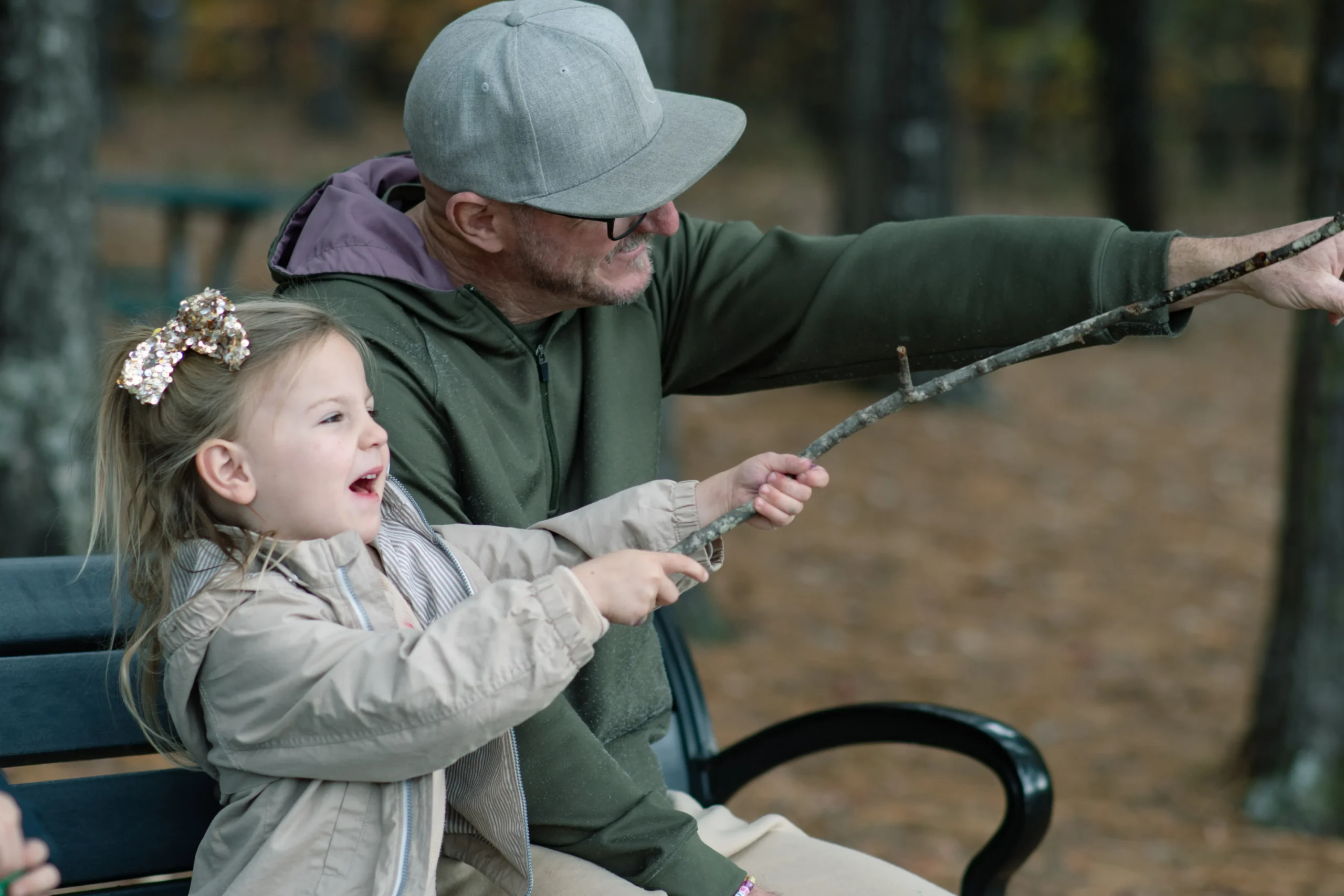 A father sits on a bench with his kids, pointing toward the trees, calm and present. The carry less standard at home.