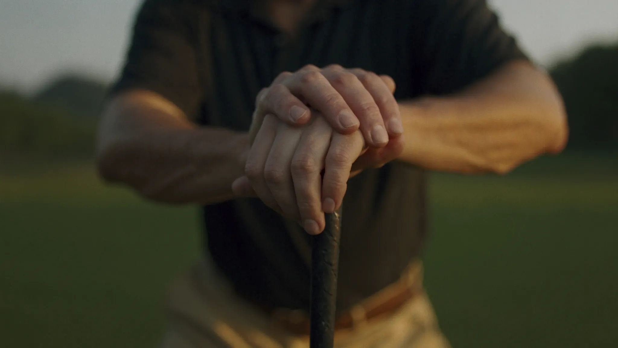 Loosening the mental grip: a man's hands resting loosely on a golf club grip in warm golden hour light